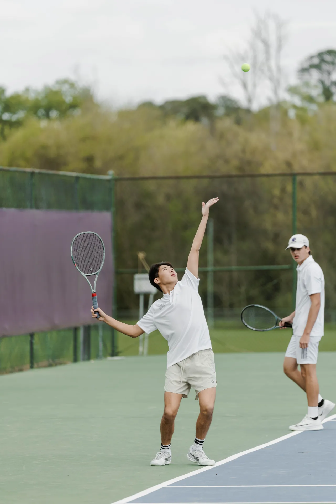 Male high school tennis player serves the ball on the tennis court