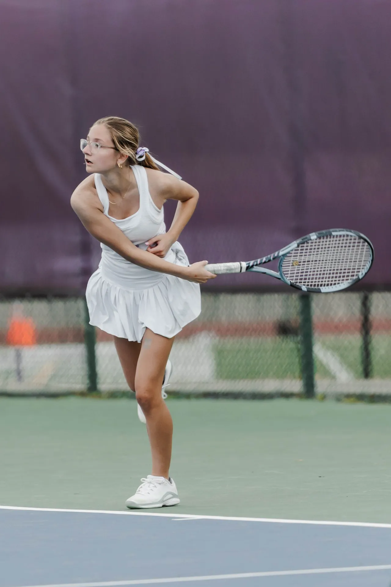 A female high school tennis player looks on after hitting the tennis ball with her racket
