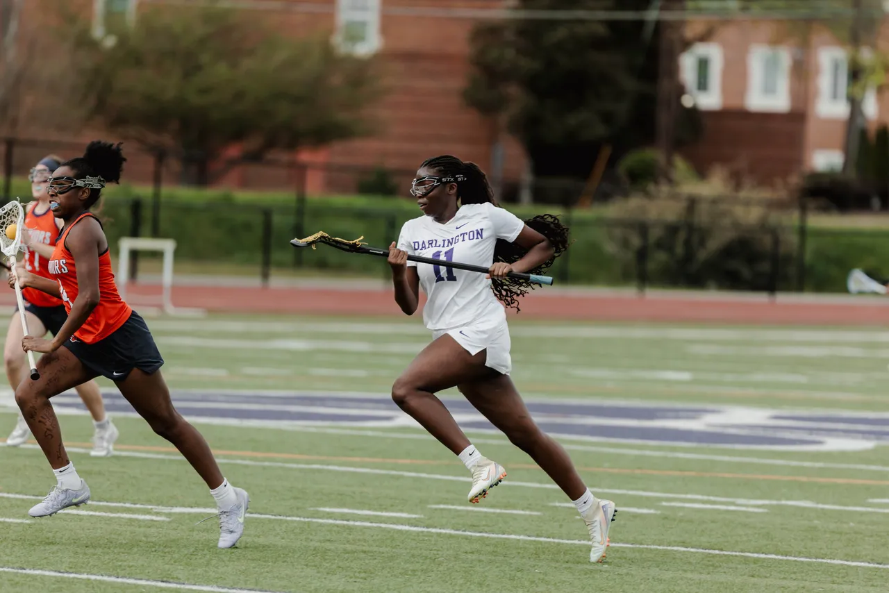 A female high school lacrosse player runs with her stick on the lacrosse field