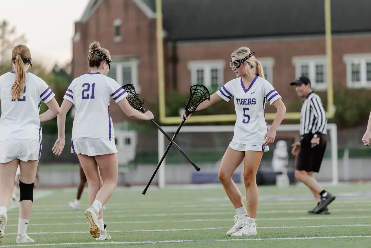 Two female lacrosse players tap lacrosse sticks on the field during a game