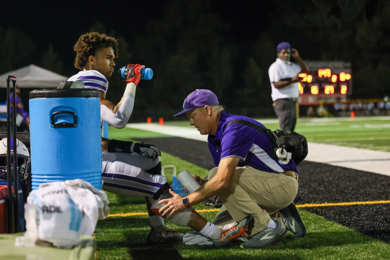Male athletic trainer assesses a football player on the sideline during a football game
