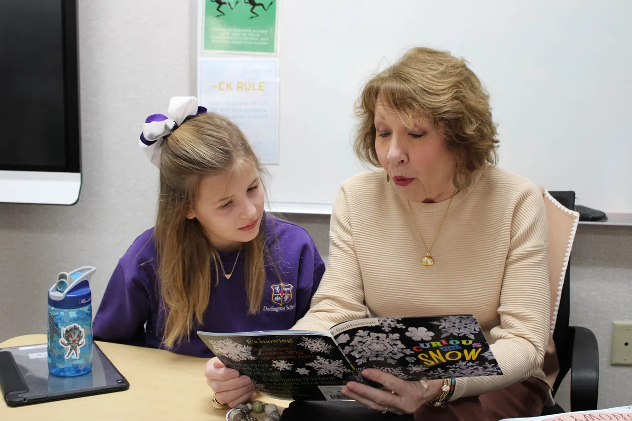 A female learning specialist reads a book to a young female student in the Teaching and Learning Center