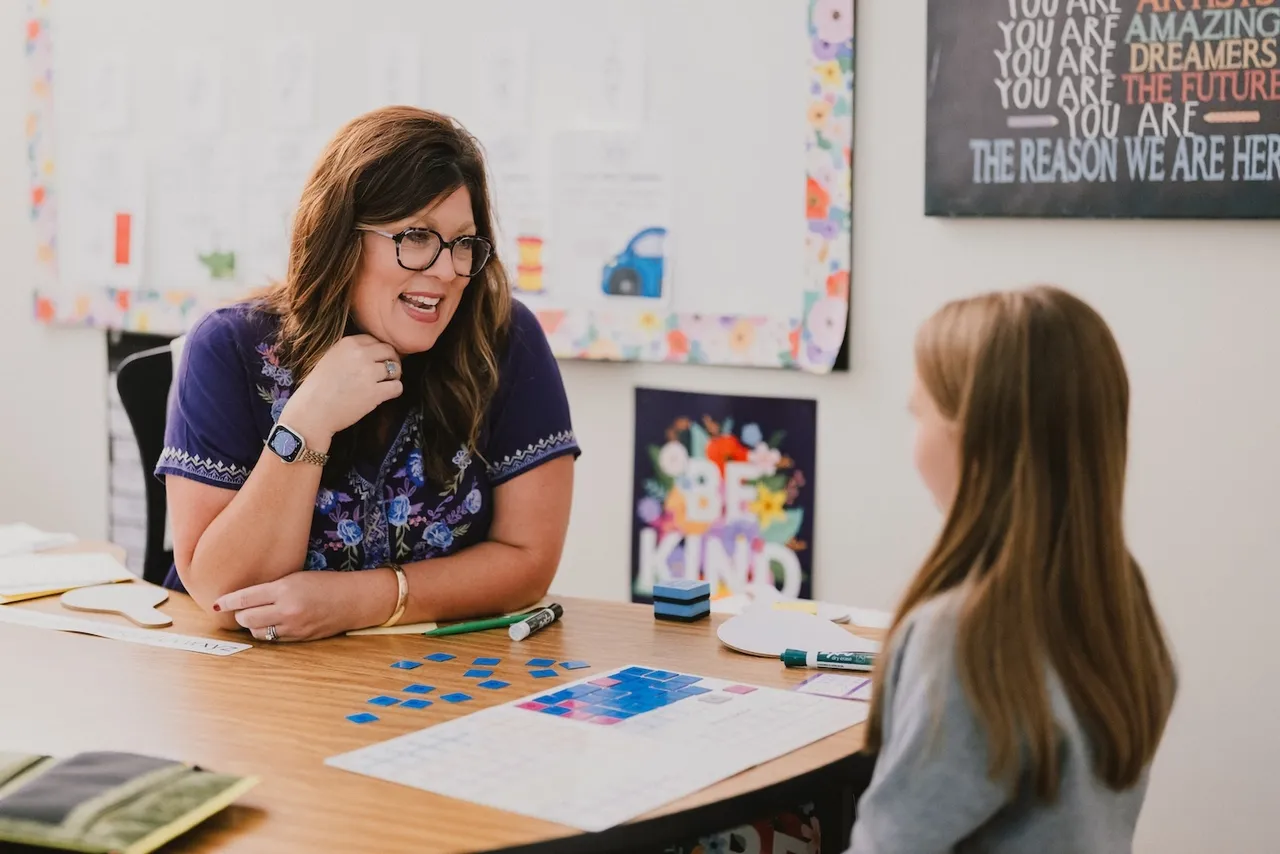 Female learning specialist works one on one with young female student on literacy