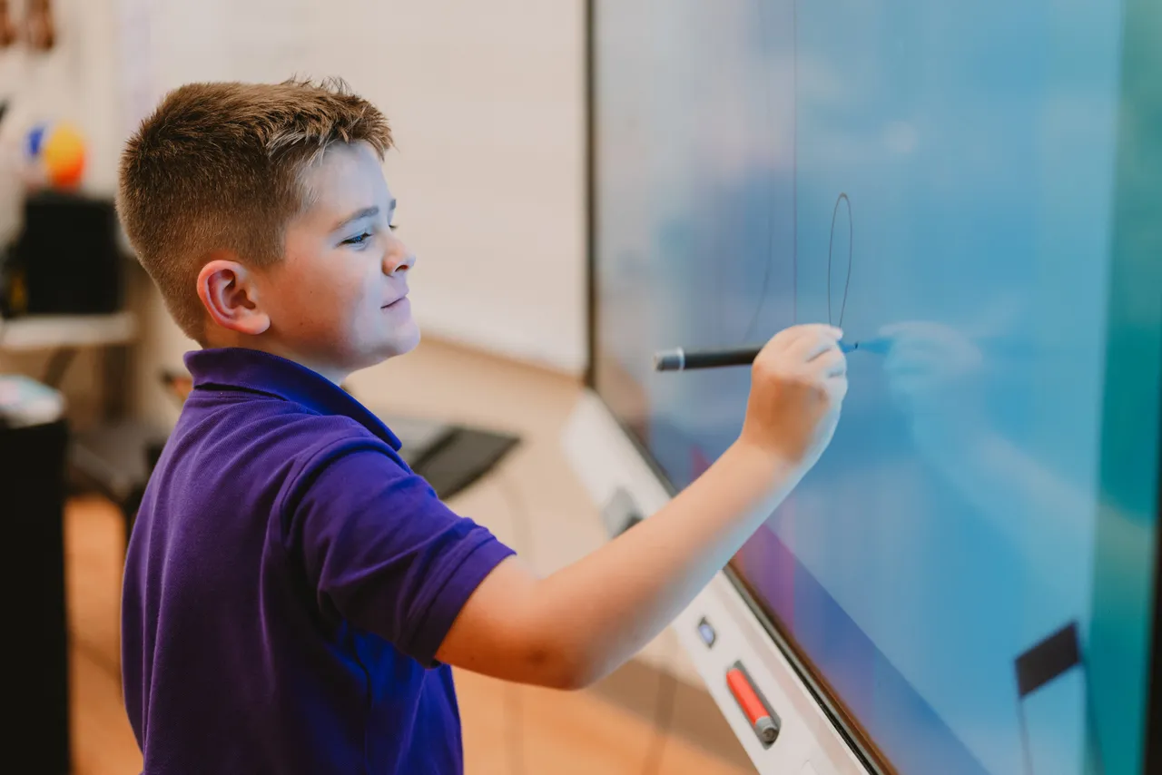 A male lower grades student writes on the smartboard during class