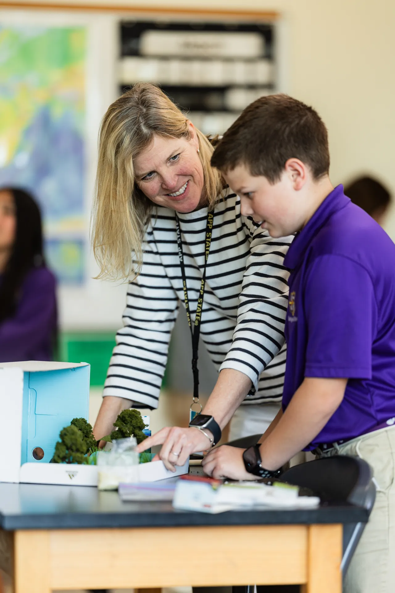A female middle school teacher works on a project with a male student in her classroom