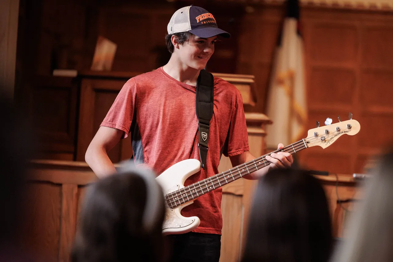A male high school student plays the guitar during a recital