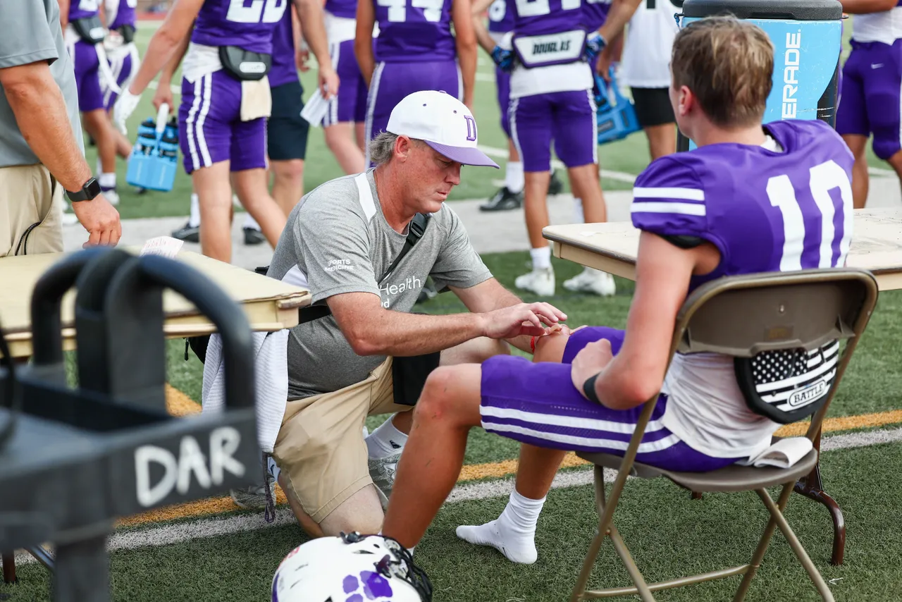 A Darlington School athletic trainer wraps a student-athlete's knee on the football sidelines.