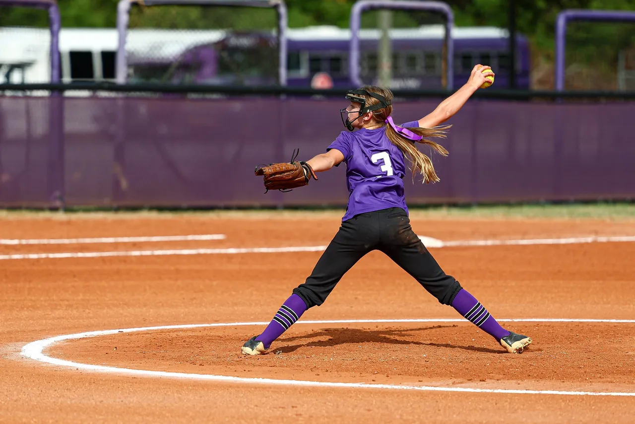 Female middle school softball player pitches the ball during a game.