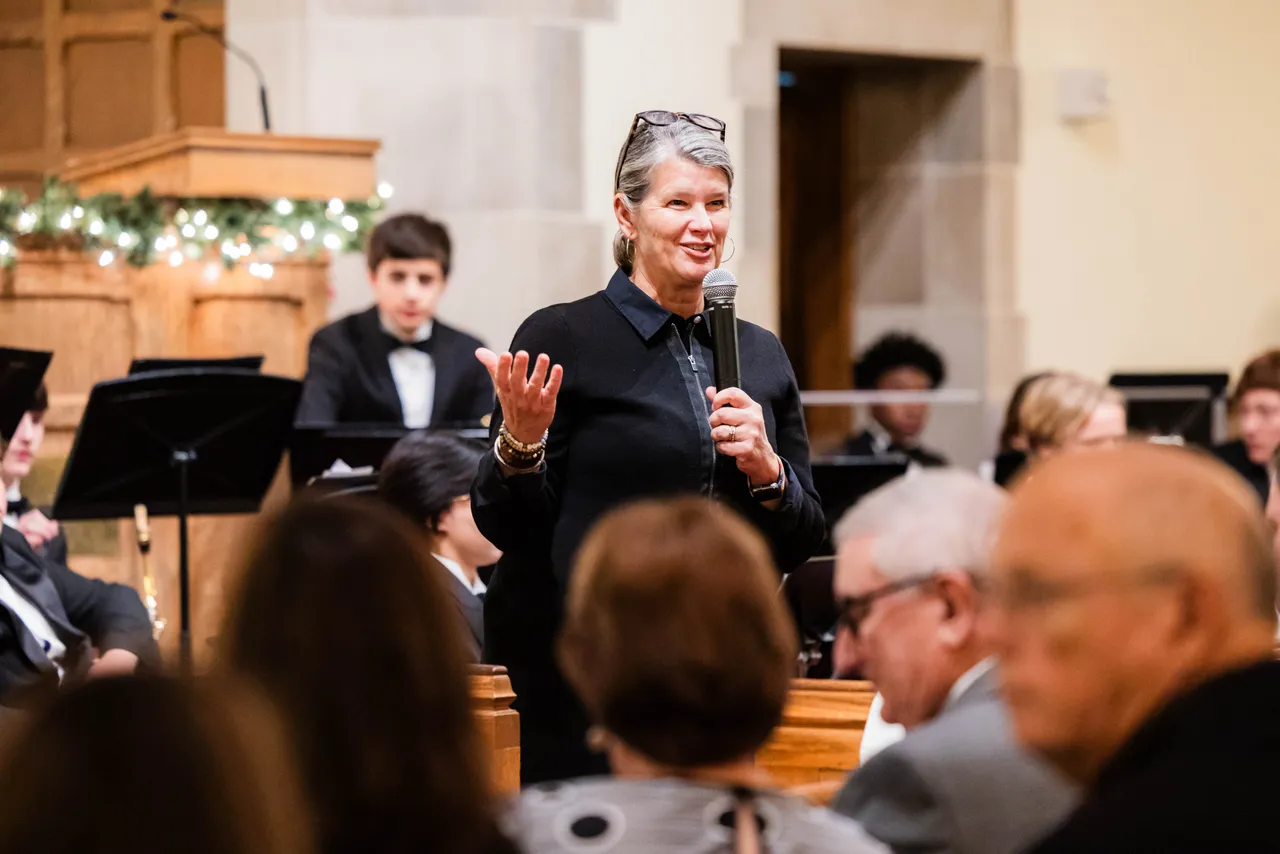 A female faculty member welcomes audience members during a performing arts concert in the chapel