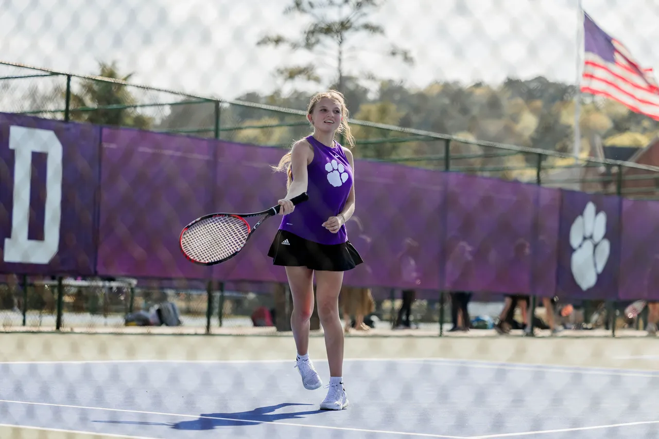 Female middle school tennis player holds a racket while preparing to hit the ball during a match.