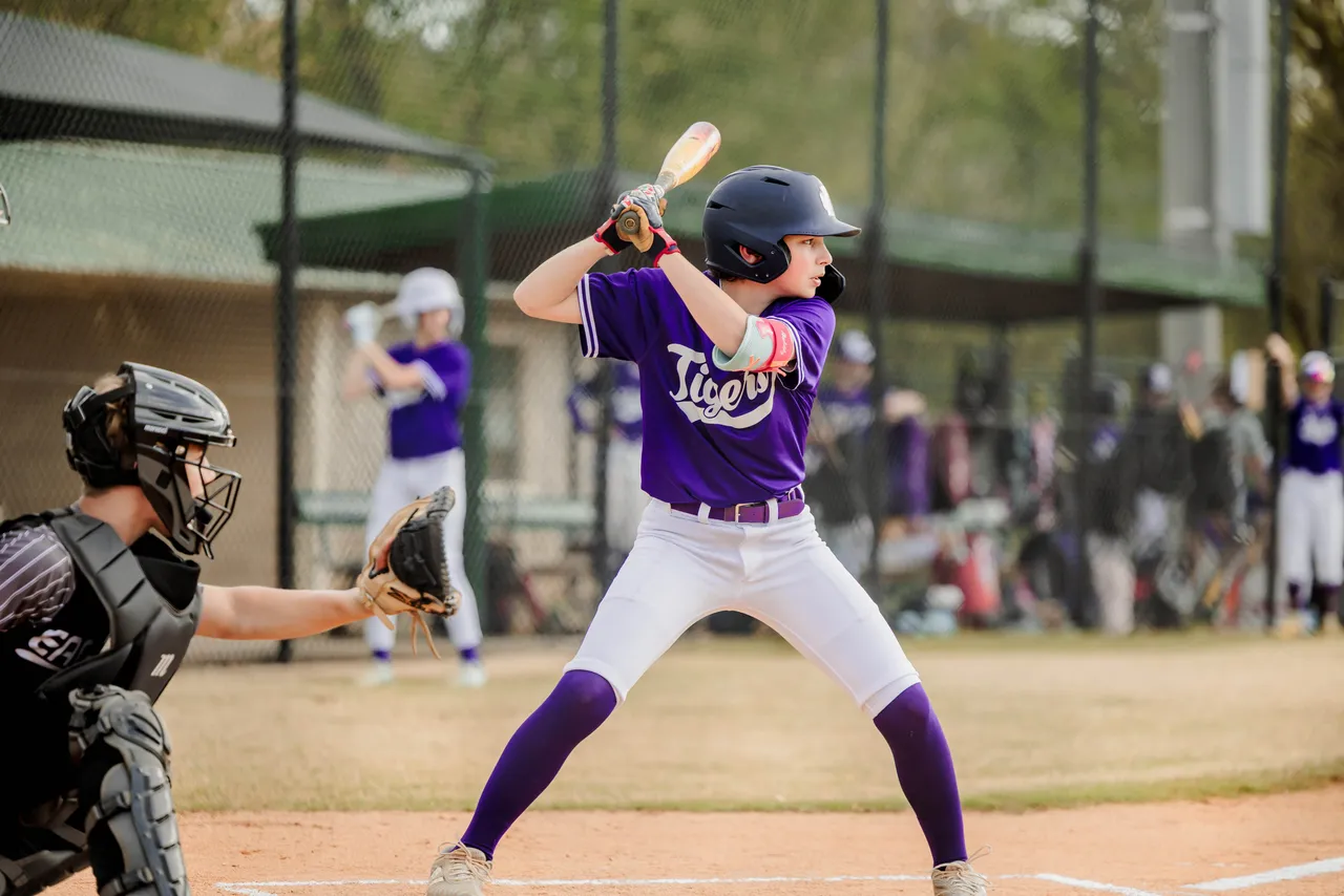 A male middle school baseball player stands at home plate preparing to hit a pitch during a game.