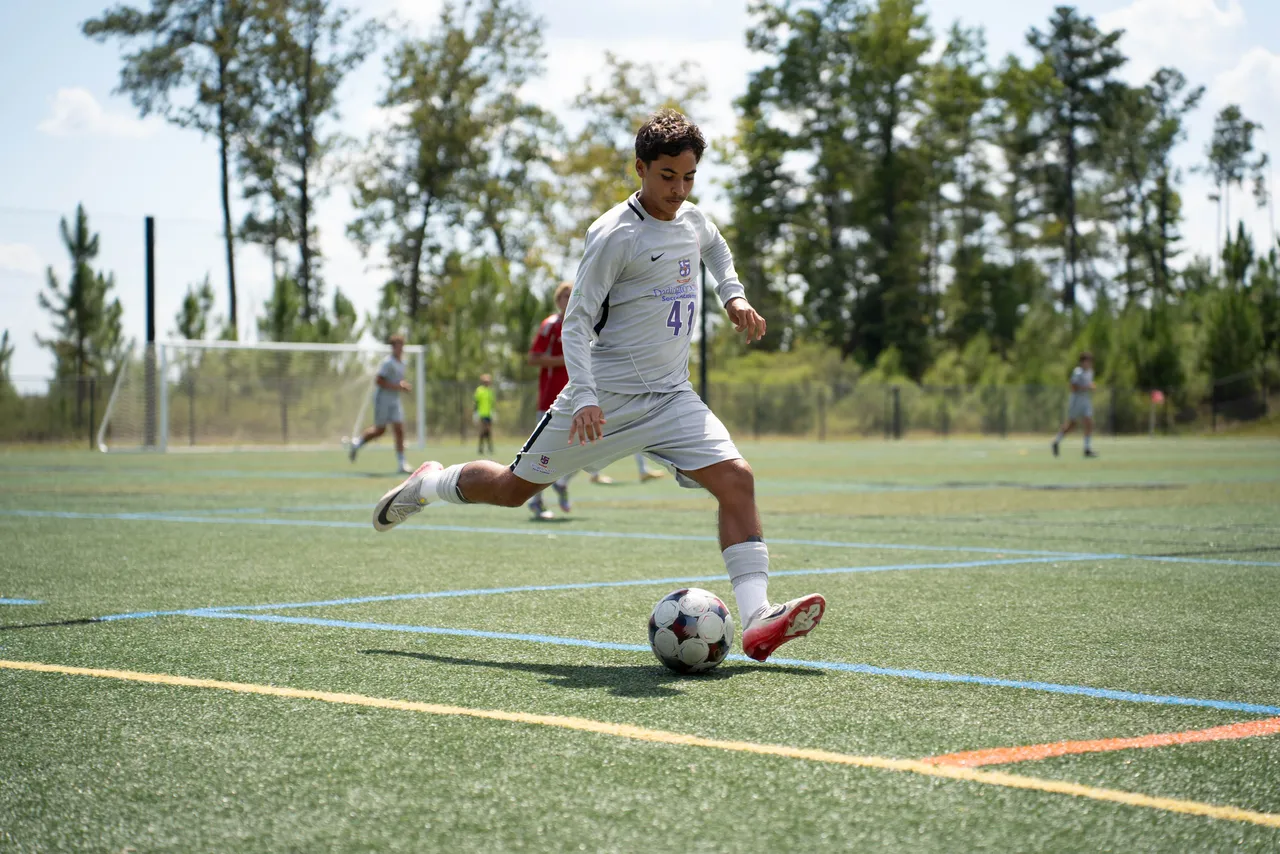 A male high school soccer player kicks the ball during a game