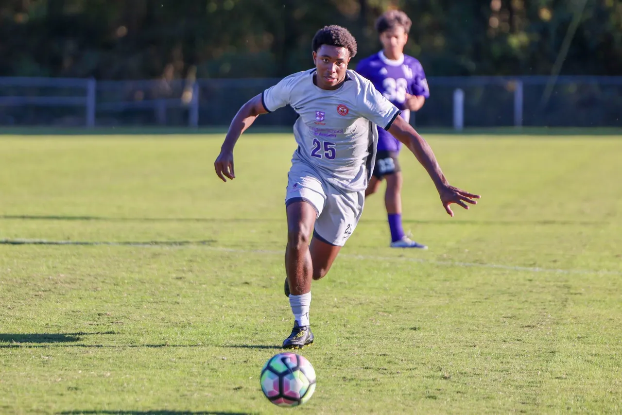 A male high school soccer player runs after the ball down the field