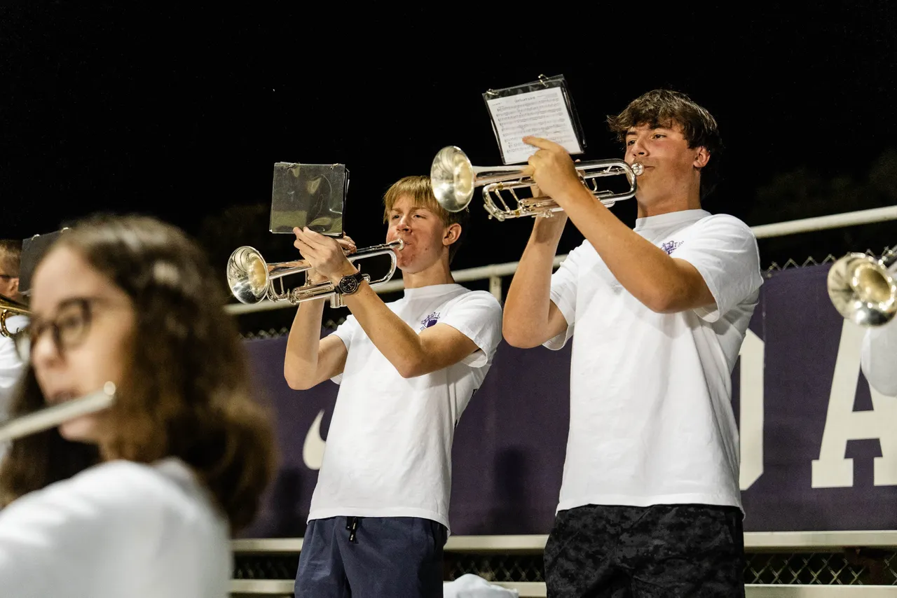 Two male Stadium Band members play the trumpet in the stands during a football game