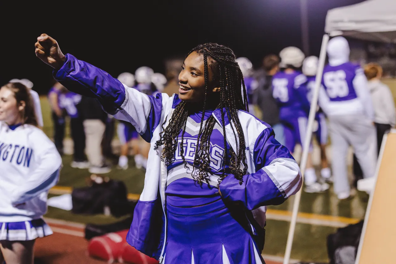 A high school cheerleader does a cheer on the sidelines during a football game