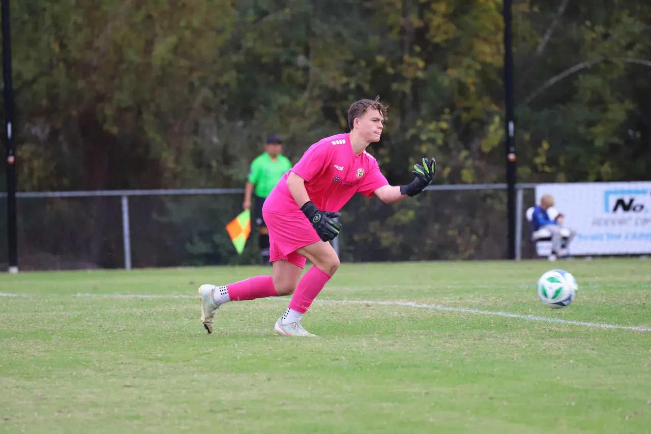A male high school soccer goalkeeper runs toward the ball