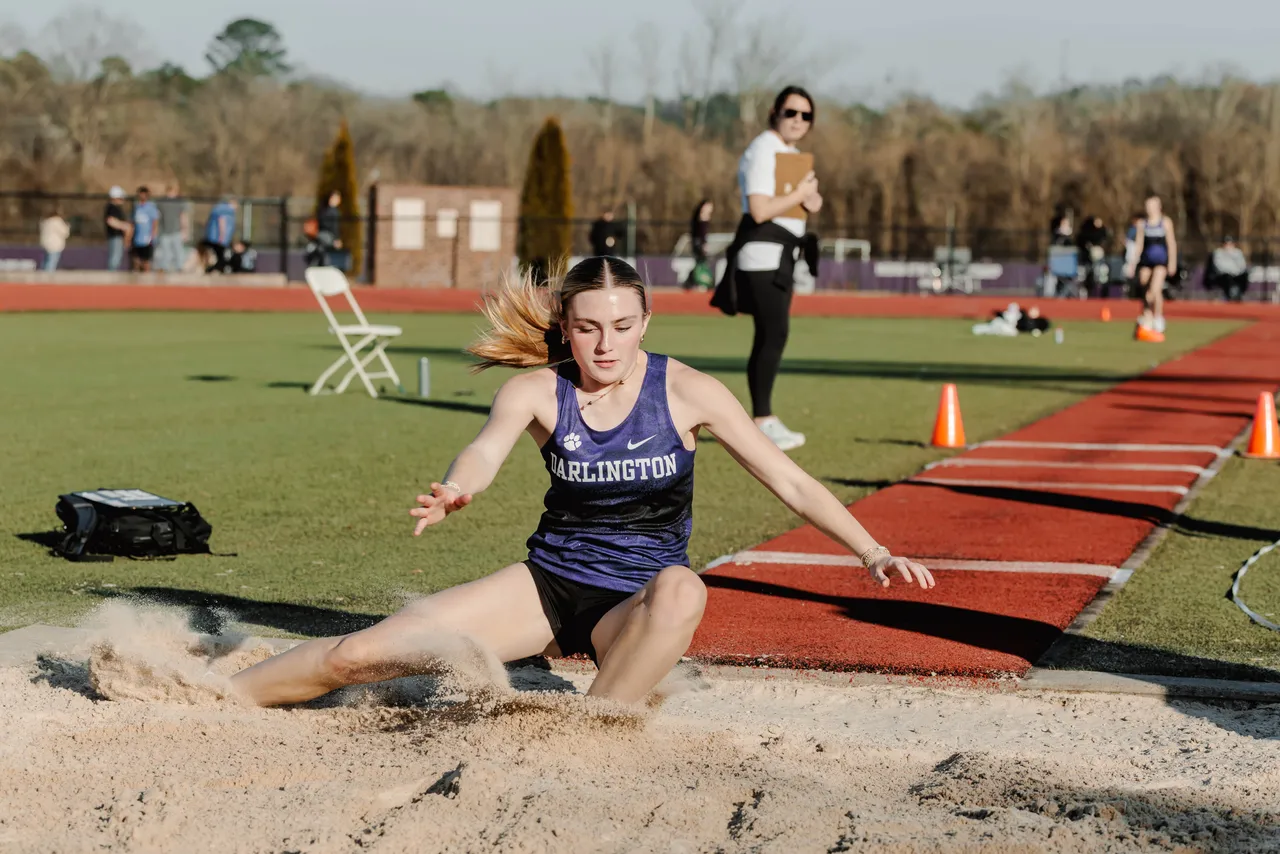 A female high school track and field team member lands in the sand after doing the long jump