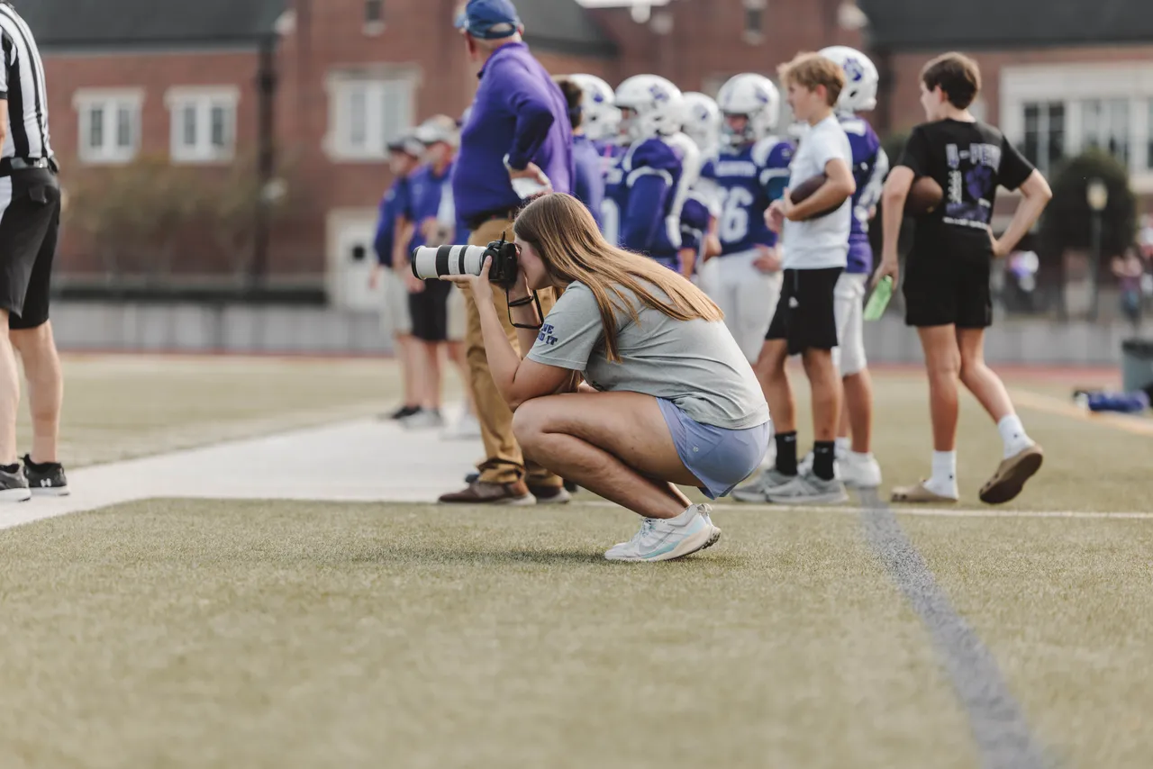 Female high school student takes photos on the sideline at a football game