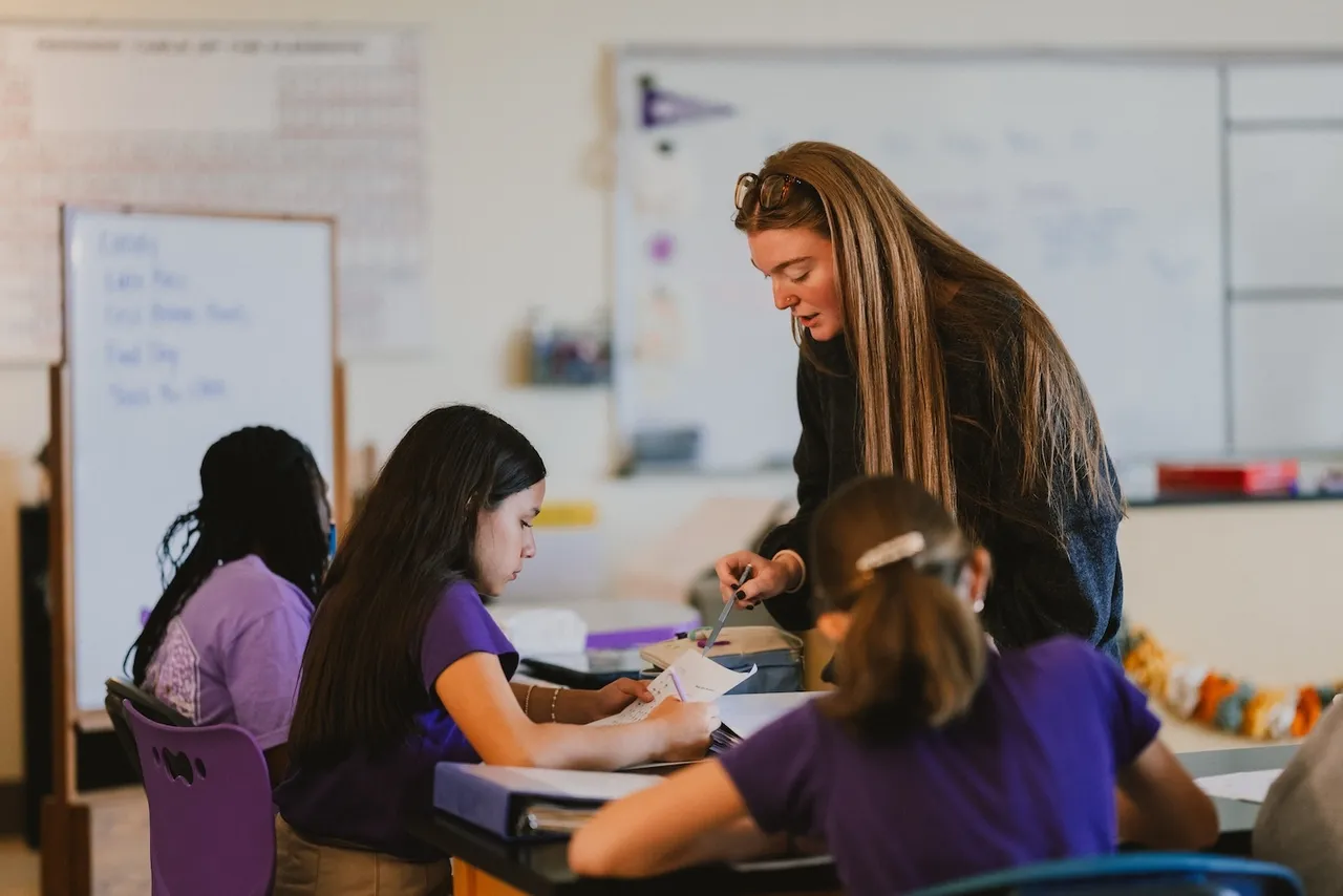 A female middle school science teacher works with two female students in her classroom
