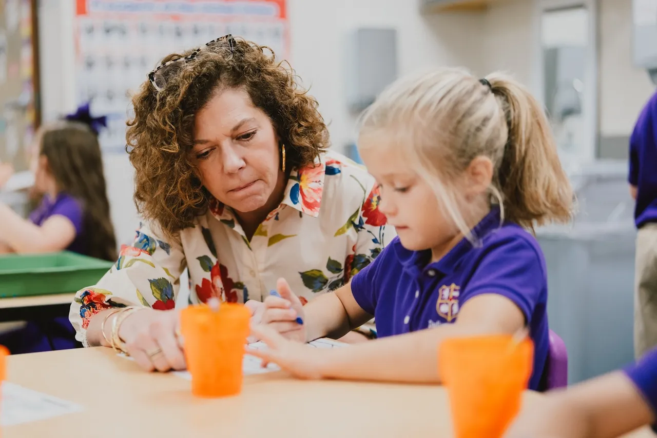 A female kindergarten teaching assistant works one on one with a female student in the classroom
