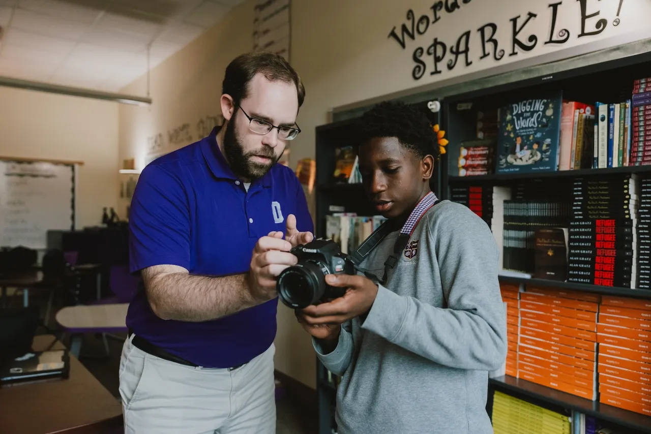A male teacher shows a male middle school student how to use a camera during photography class