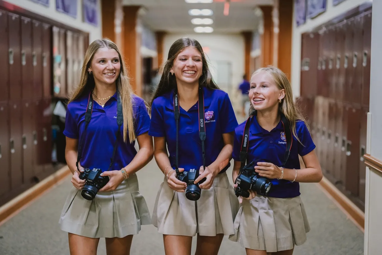 Three female middle school students walk down the hallway with their cameras as they look for photos to take during photography class