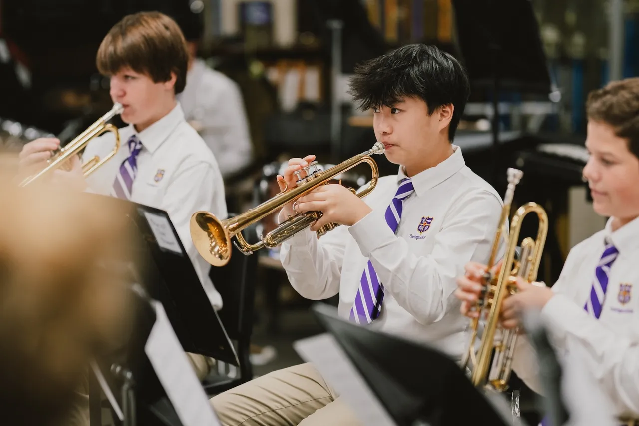 Three male band students play brass instruments during rehearsal