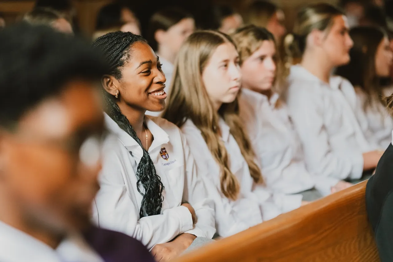 Female high school students sit together watching a presentation during weekly chapel