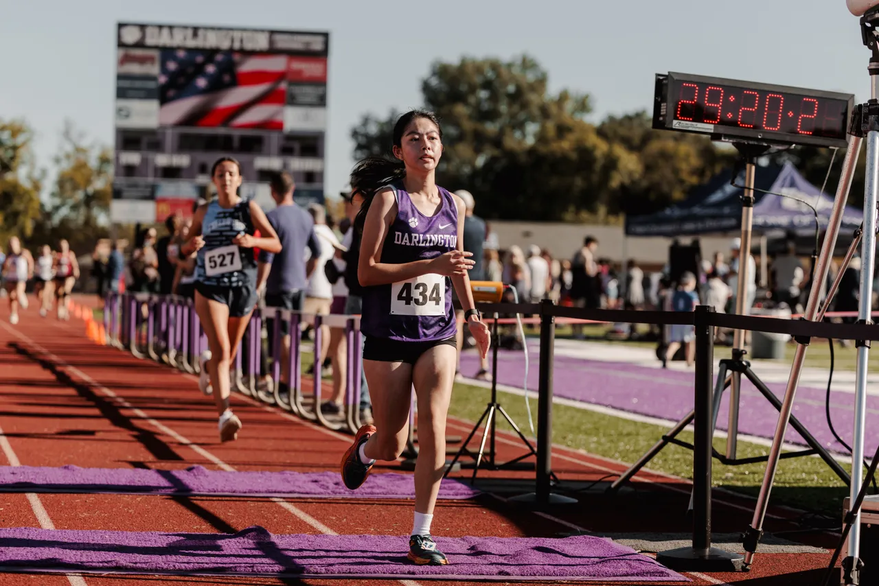A female JV cross country runner crosses the finish line during a race.