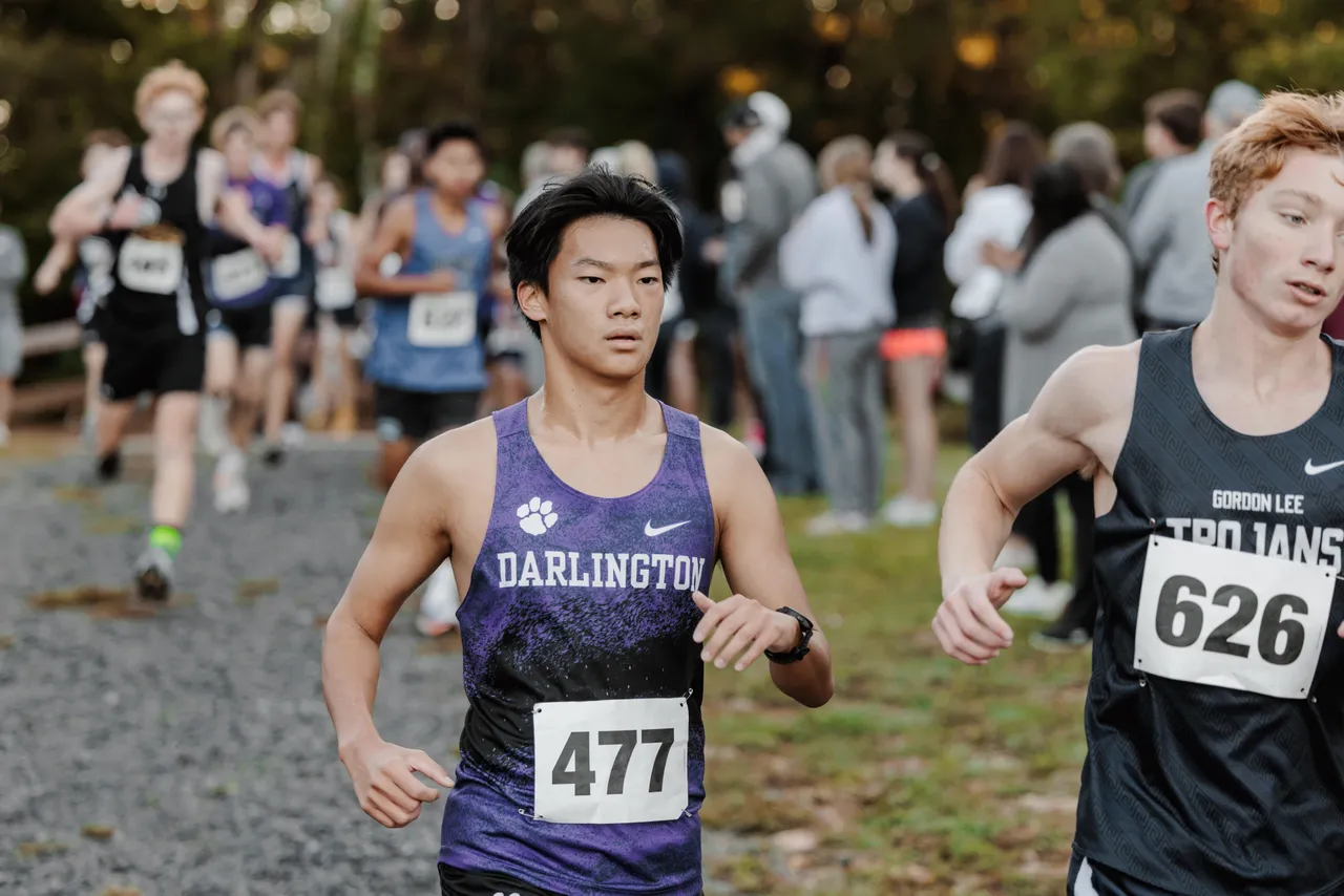 A male varsity cross country runner competes in a race alongside another runner.