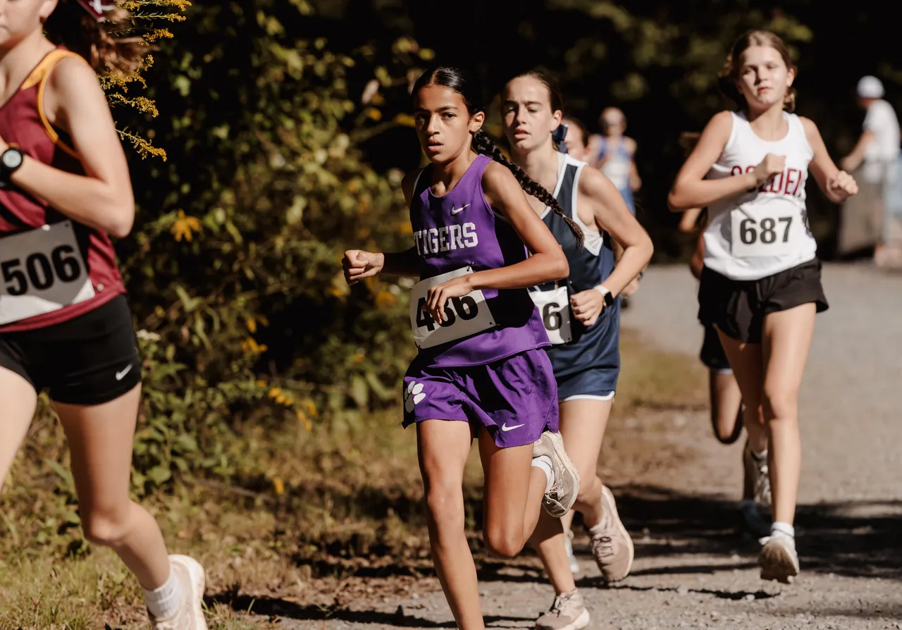A female middle school cross country runner competes alongside other runners during a race.