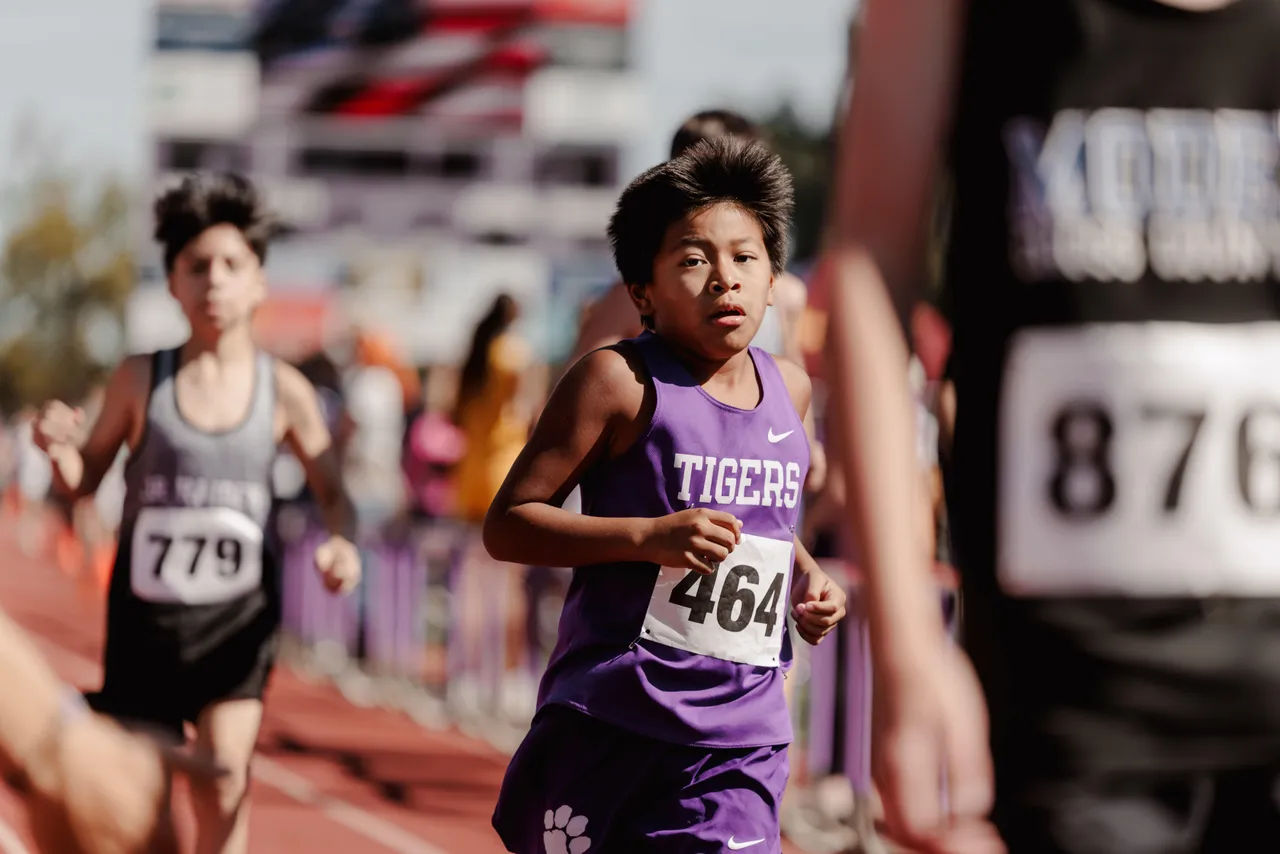 A male middle school cross country runner competes alongside other runners during a race.