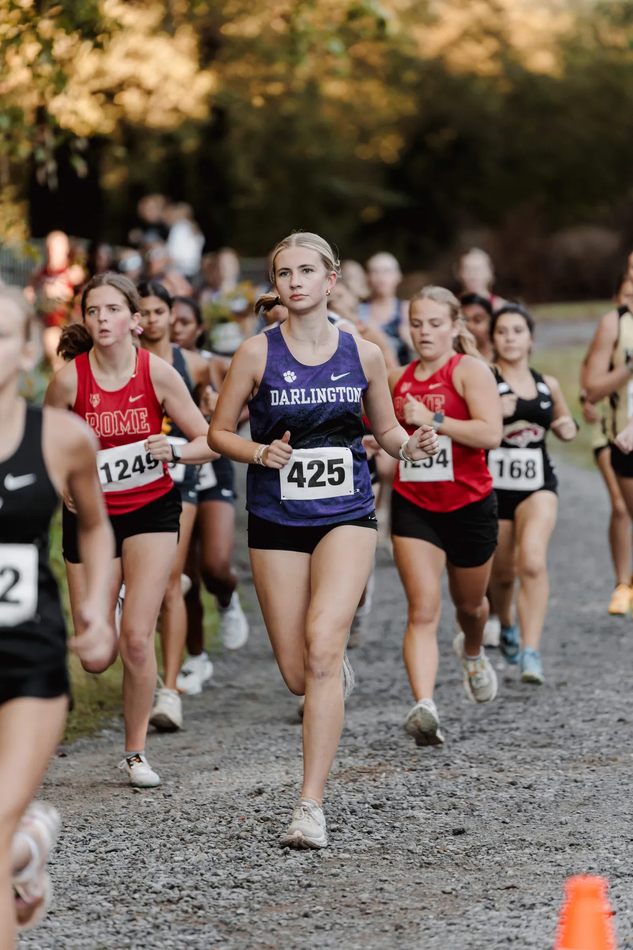A female varsity cross country runner competes in a race alongside other runners.