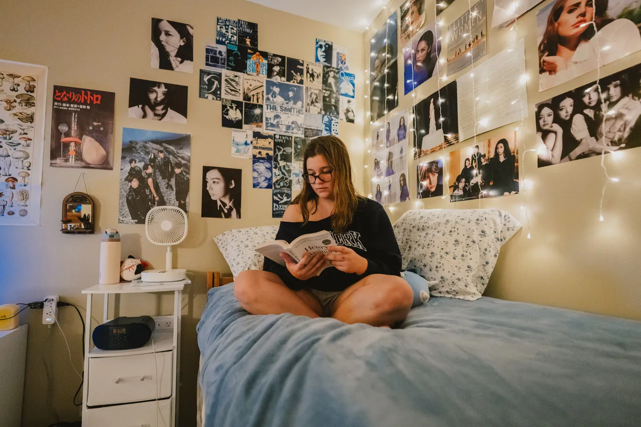 Female boarding student reads a book on her bed in her dorm room