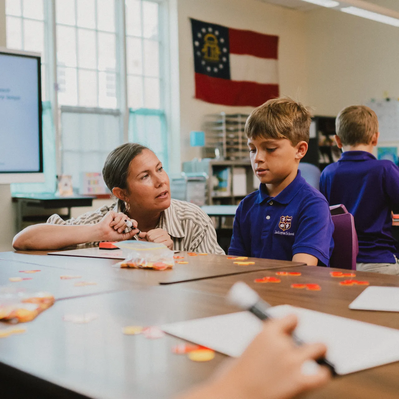 Female teacher working with a young male student in a classroom.