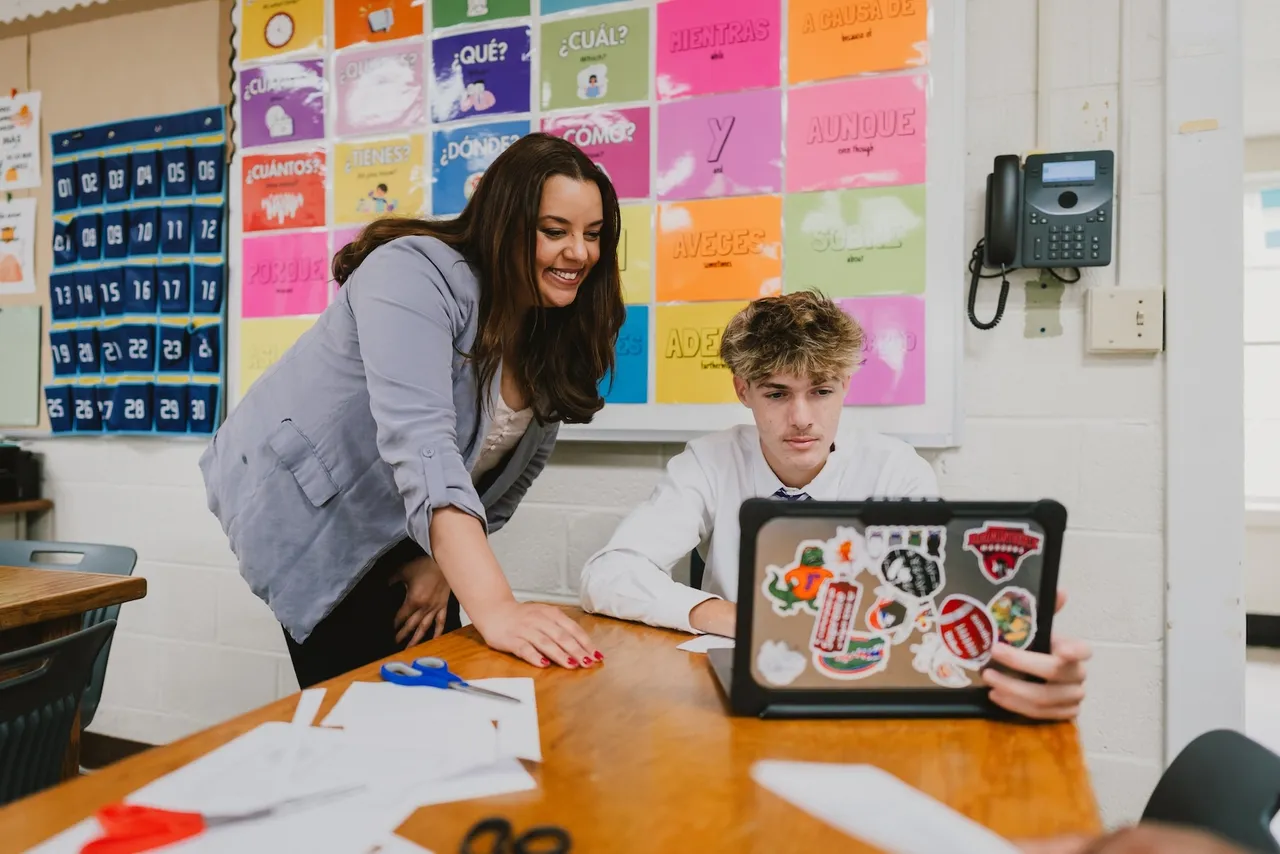 A female teacher works with a male student on his laptop in her Spanish classroom