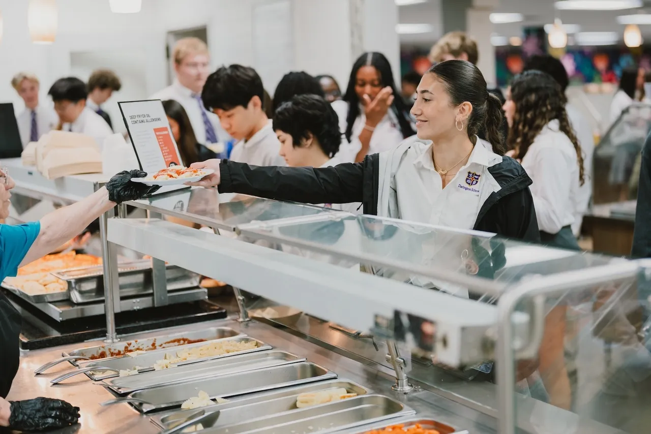 Female high school student is handed a plate of food from the hot line in the dining hall