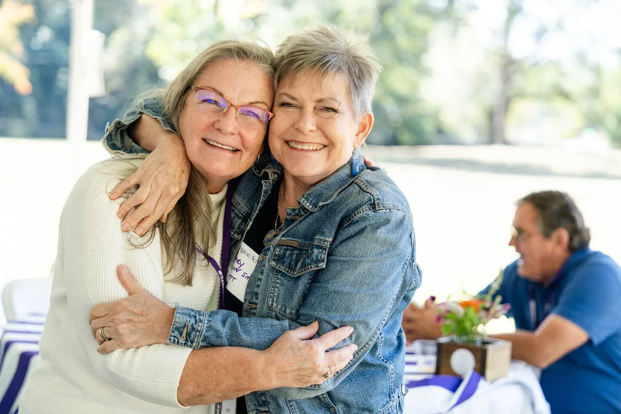 Two female alumni smile and hug at a Darlington School alumni event.