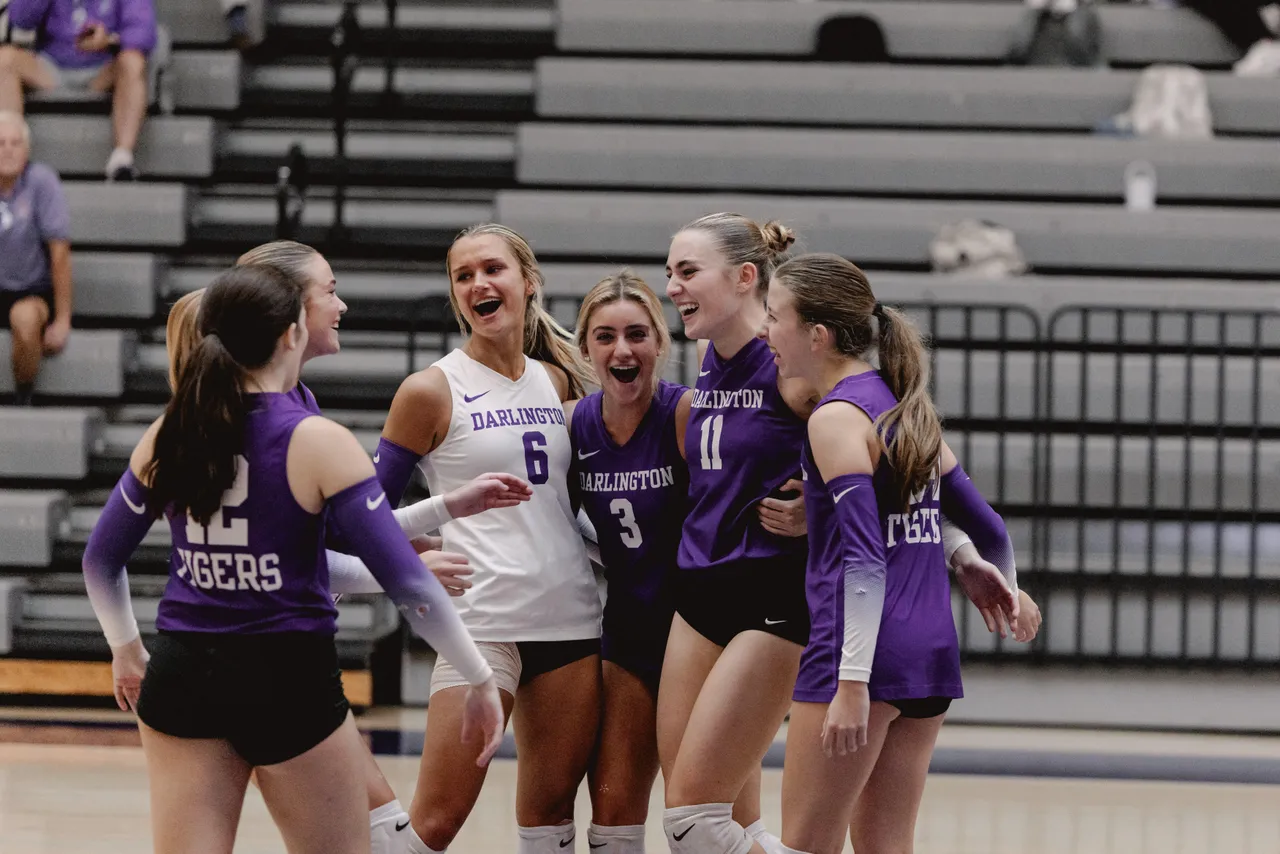 Six female volleyball players embrace with smiles on their faces