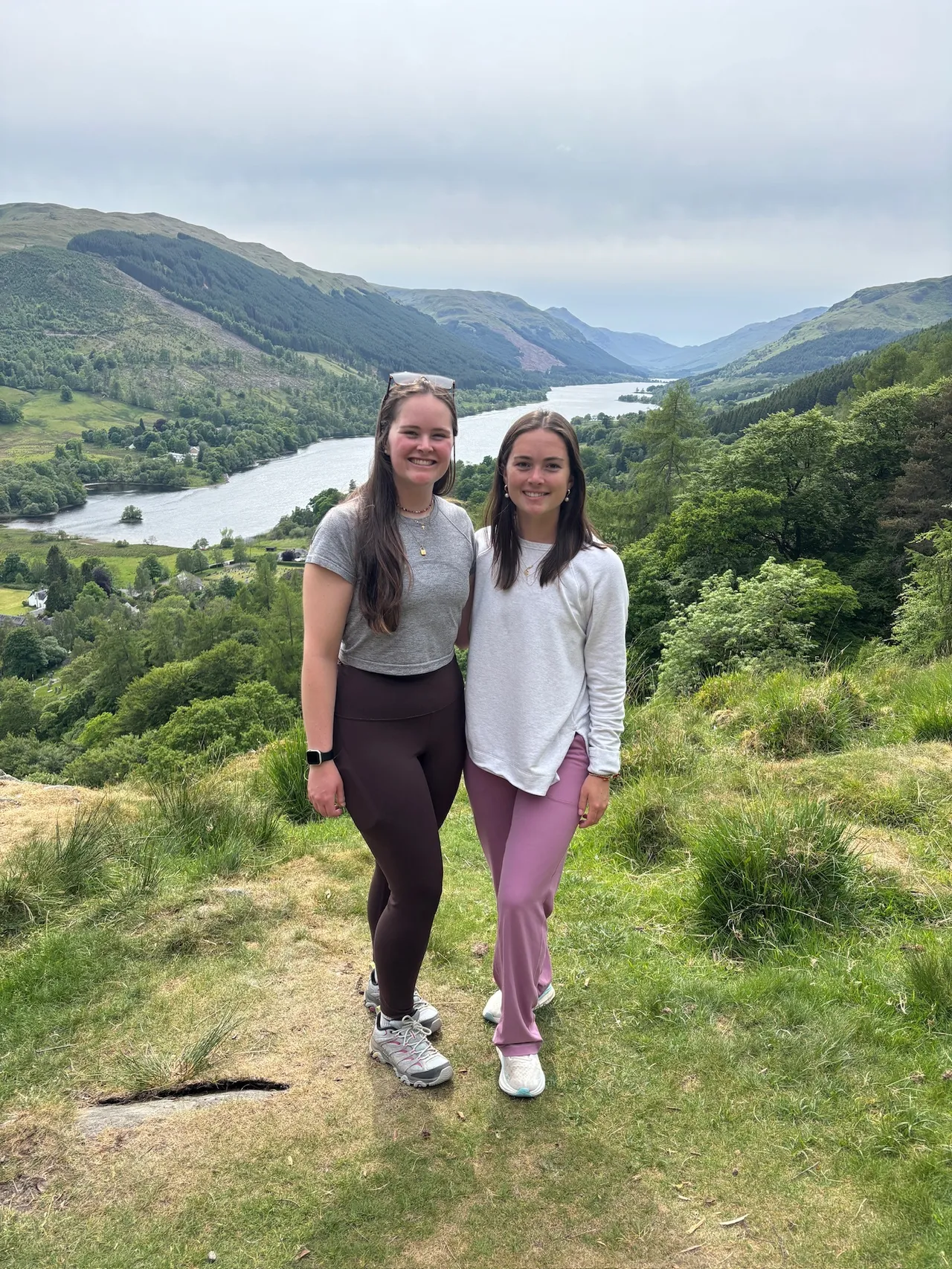 Two female young alumni pose outdoors in front of mountains and a river