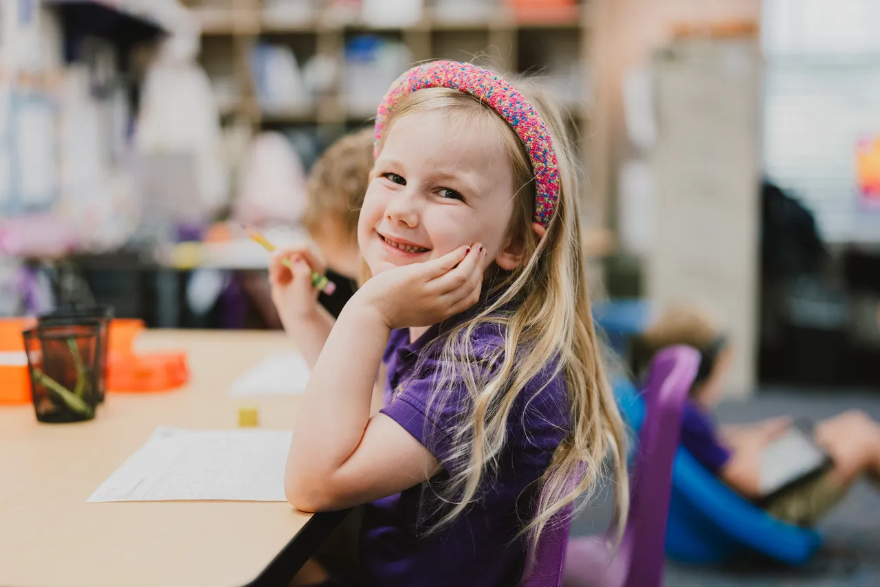 Female primary grades students works on a writing activity in her classroom while smiling