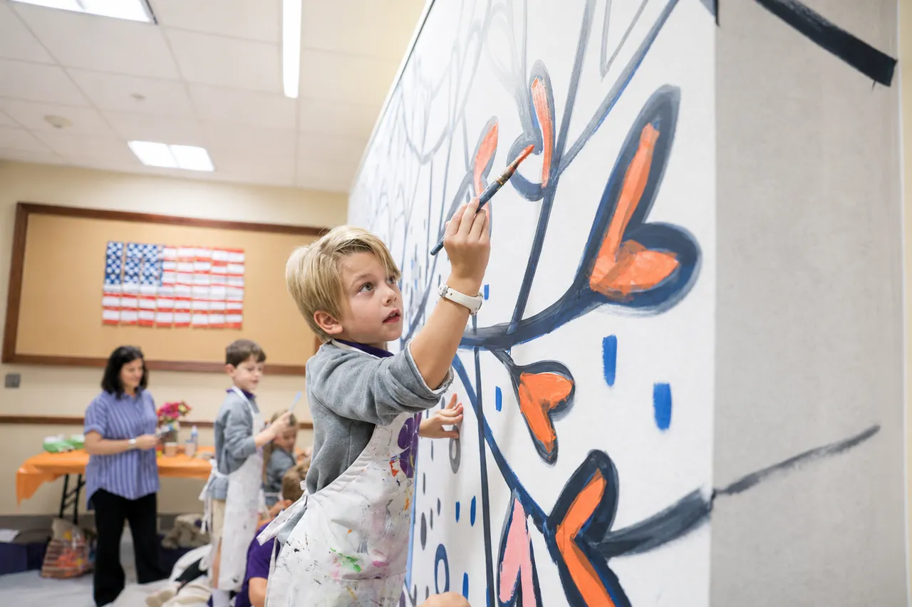 A male lower grades student paints a mural with help from classmates during art class
