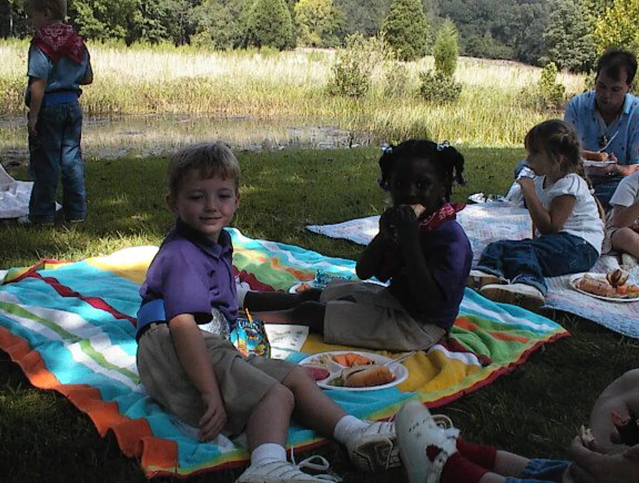 Pre-kindergarteners Biddy Braden and Kelsey Garrett enjoy lunch by a creek during Wild West day at a local farm.