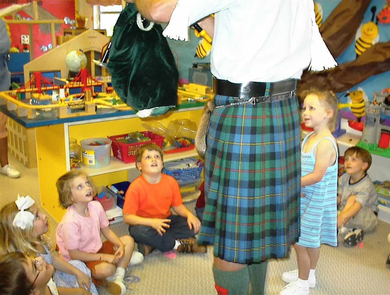 Pre-kindergarteners watch and listen as Darlington friend, Scott Macleod, fashions a kilt and plays the bagpipe.