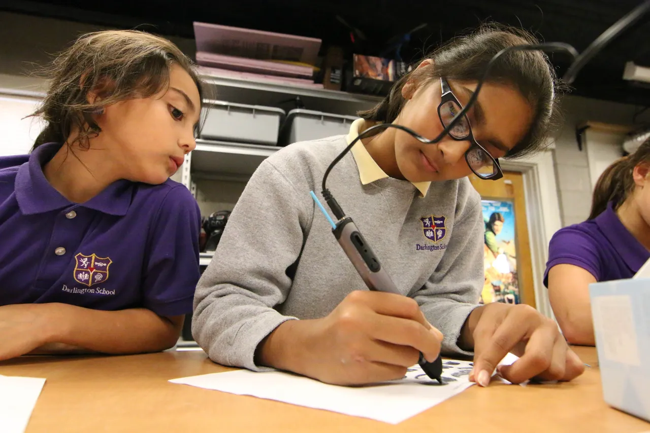 Sixth-grader Sia Patel creates a design with a 3Doodler pen as second-grader Shyann Wardlaw looks on.