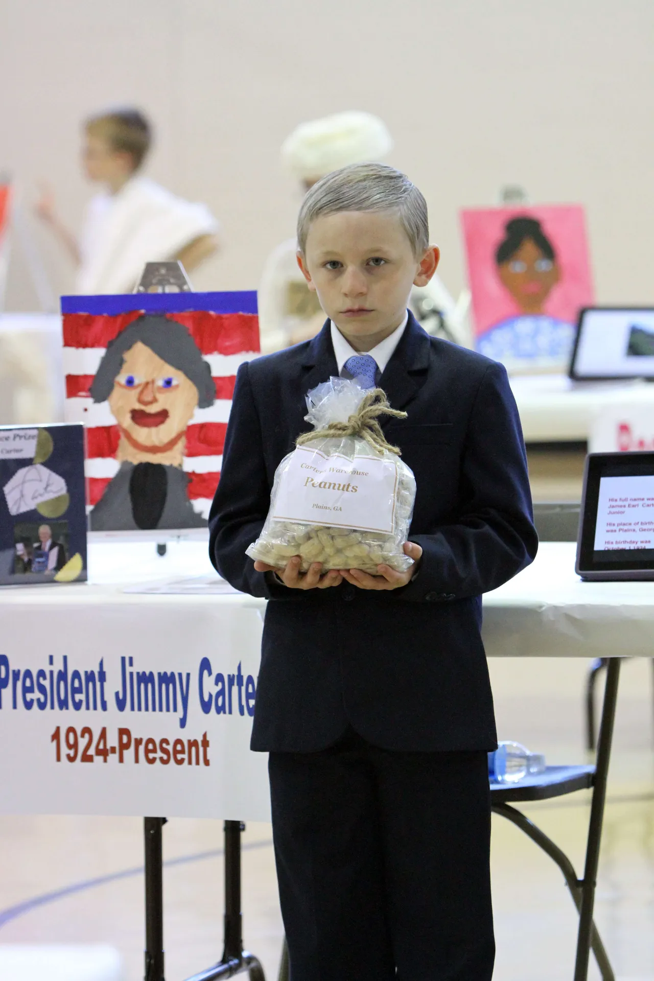 Third-graders completed research and made Keynote presentations and iMovie videos about their historical fiction, all under the tutelage of the fourth grade. A walk-through-history wax museum project is an old-school biography project overhauled for the 21st Century by third-grade teacher Steve McConnell. The project was also multi-disciplinary as students drew a self portrait, researched and wrote a paper, acted like their characters, and translated basic parts of the project into Spanish. Here, Aiden Cloud (’21) poses as Jimmy Carter.